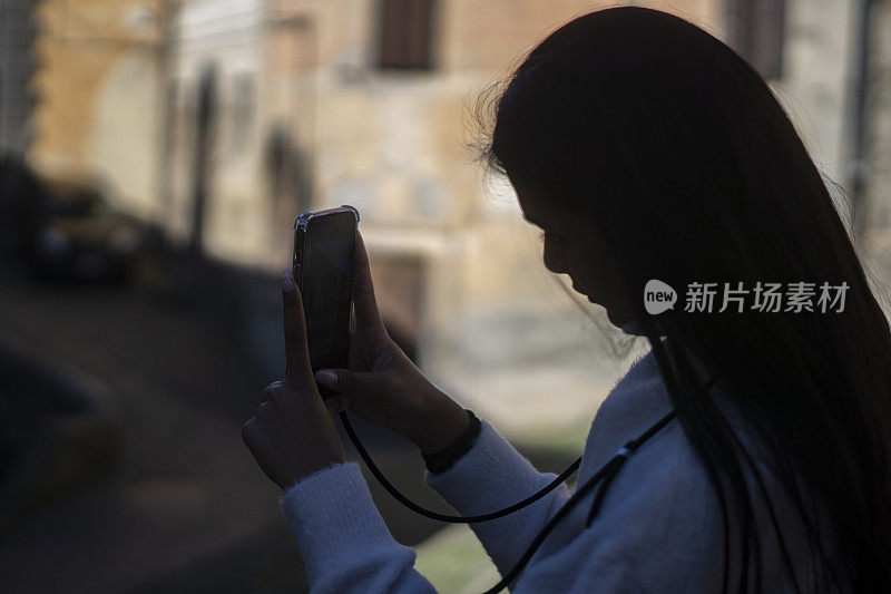 一个年轻女子的剪影在外面用她的智能手机拍照。