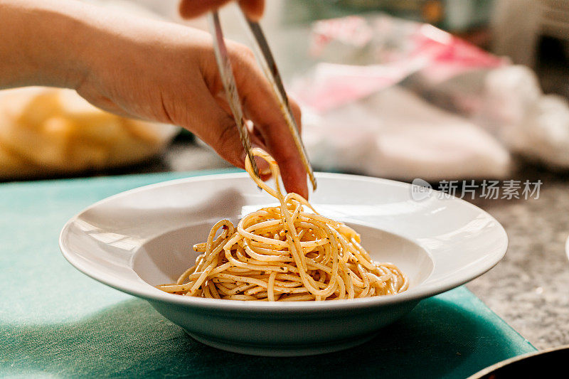 厨师的手很小心，把意大利面放在一个白色的盘子里