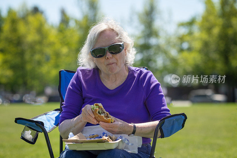 夏天，老妇人在公园吃外卖汉堡