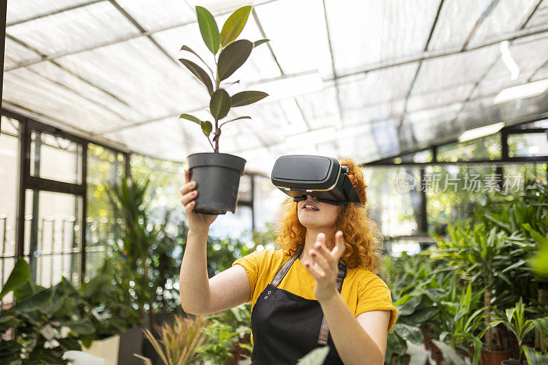 戴着vr眼镜在花店工作的年轻红发女子手持植物