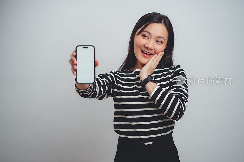 一名亚洲女性开心地笑着，智能手机上的白色屏幕孤立地站在白色背景上。