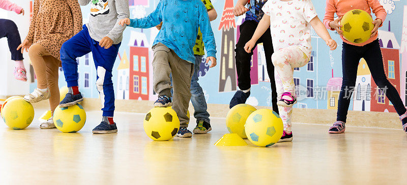 幼儿园的孩子们在上足球课。一群拿着泡沫足球的孩子站成一排，踢着球。幼儿园体育足球训练