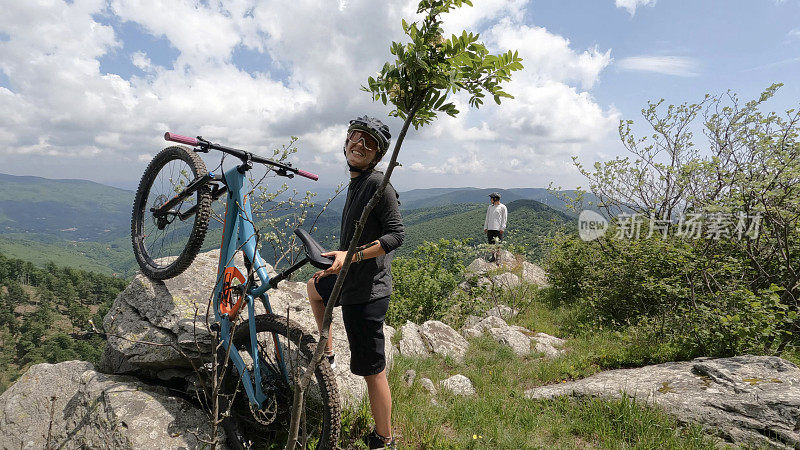 山地自行车手推着自行车俯瞰山谷、森林