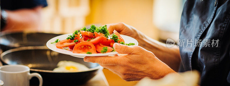 手里拿着一盘健康的西红柿，欧芹番茄沙拉