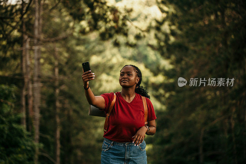 一名非裔美国妇女站在瀑布边用智能手机欣赏山间美景。