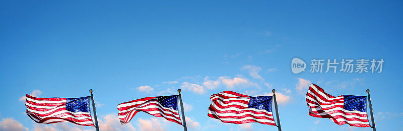 在晴朗的天空上，旗杆上的美国国旗排成一排