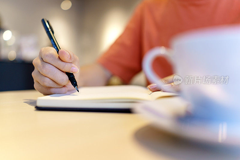 一个亚洲女人坐在桌旁，手里拿着笔和个人记事本。她在她面前的文件上做笔记，专注于她的任务。