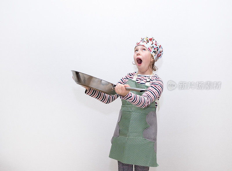 一个8岁的白人女孩打扮成厨师，手里拿着一个大煎锅，她很惊讶。