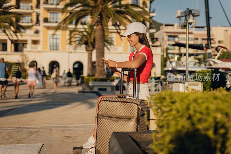 一名女子在地中海港口提着行李箱使用智能手机