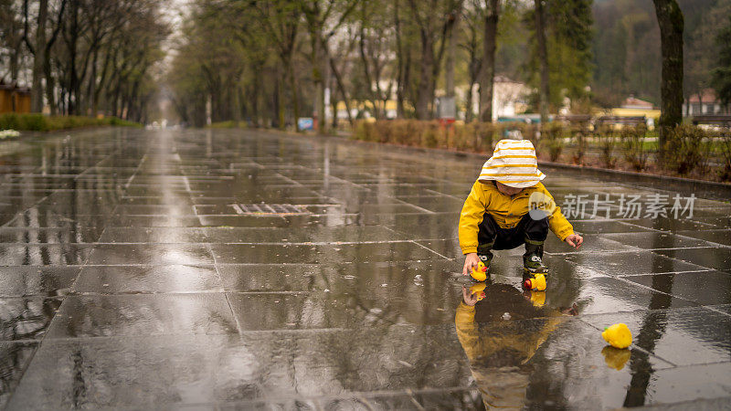 漂亮有趣的金发小孩带着橡皮鸭，在水坑里跳跃，在雨中玩耍