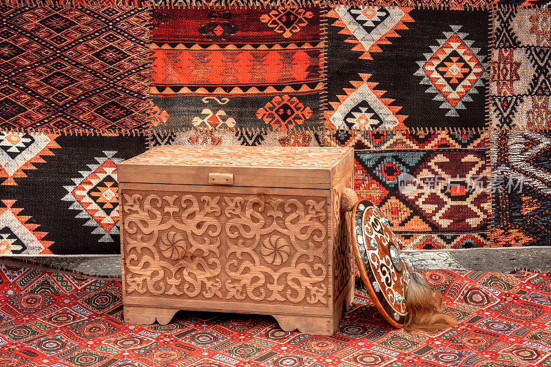 传统的亚洲木制箱子，上面有雕刻的装饰品，背景是蒙古包里的地毯——游牧民族的住所。特写镜头