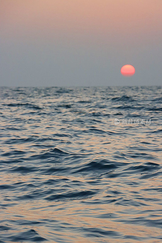 红色的太阳在海洋地平线上戏剧性的橙色天空中落下，忧郁的灰色云岸，海上的波浪，波涛汹涌的水面，复制空间