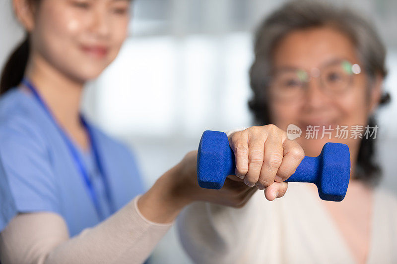 亚洲女医生建议老年病人到物理治疗师家里用哑铃锻炼。微笑的护士帮助老年病人锻炼，使肌肉强壮。理疗师护理。