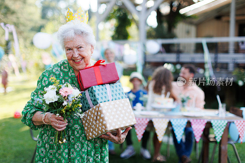 大寿女子手持礼物和花束的肖像。老夫人的花园生日派对。