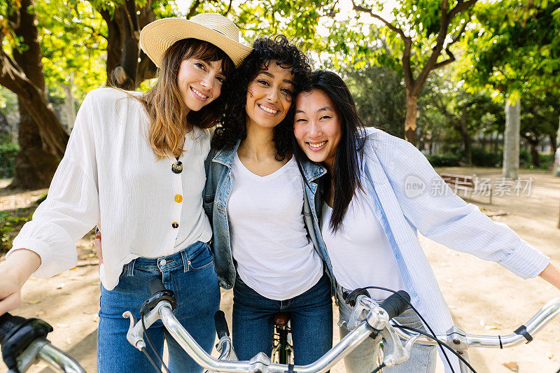三位千禧一代的年轻女性朋友站在户外，骑着自行车