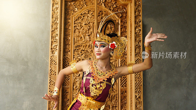 巴厘女孩穿着巴厘传统服饰，用王冠、珠宝和金饰饰品装点门面，以巴厘图案为背景