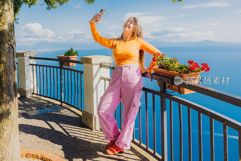 快乐的女人用智能手机自拍，欣赏着田园诗般的海岸美景