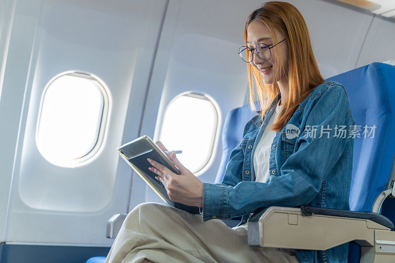 快乐的年轻女子在飞机上独自坐在窗边玩着她的平板电脑