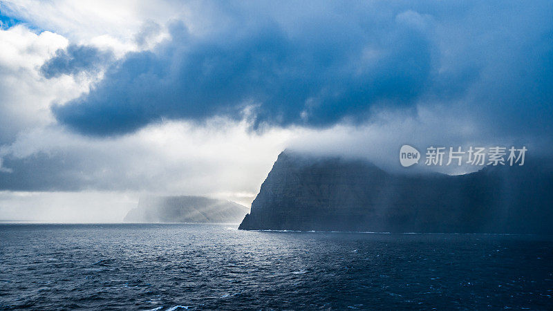 法罗群岛的海景从渡轮在波浪的水域。暴风雨天气，有很大的云景和一些阳光。