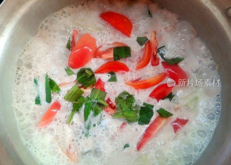 在煮椰奶汤中加入番茄片——泰国菜的准备。