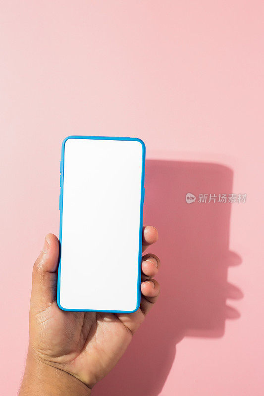 垂直镜头:一只手拿着一部粉色背景、空白屏幕的蓝色智能手机