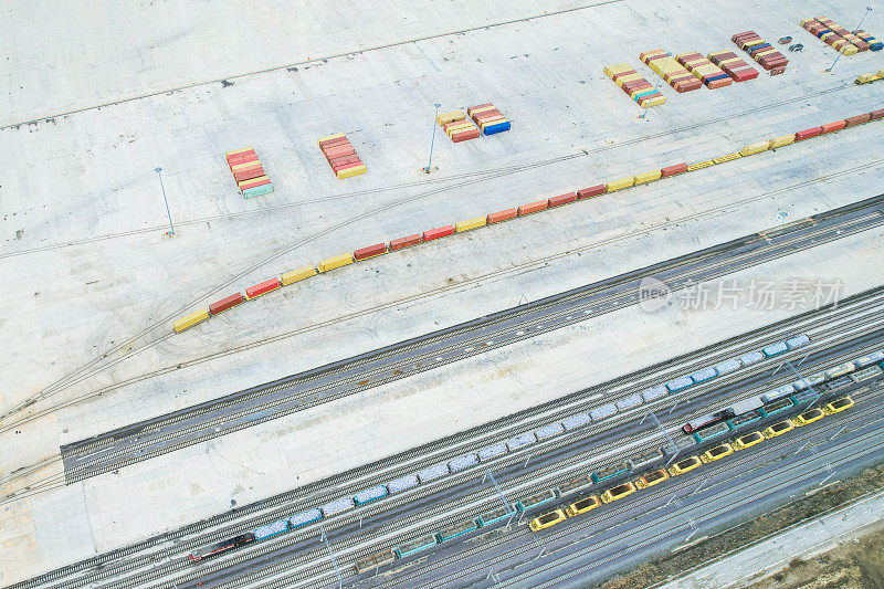 货运列车载着货运集装箱，背景中有成排的集装箱，无人机视图