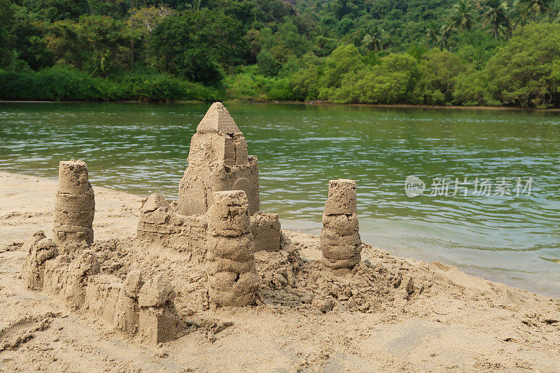 在印度果阿的海滩上建造的复杂沙堡堡垒的图像，用桶和铲子制成，并修改为围绕外部的墙，背景是大海，抬高的视野