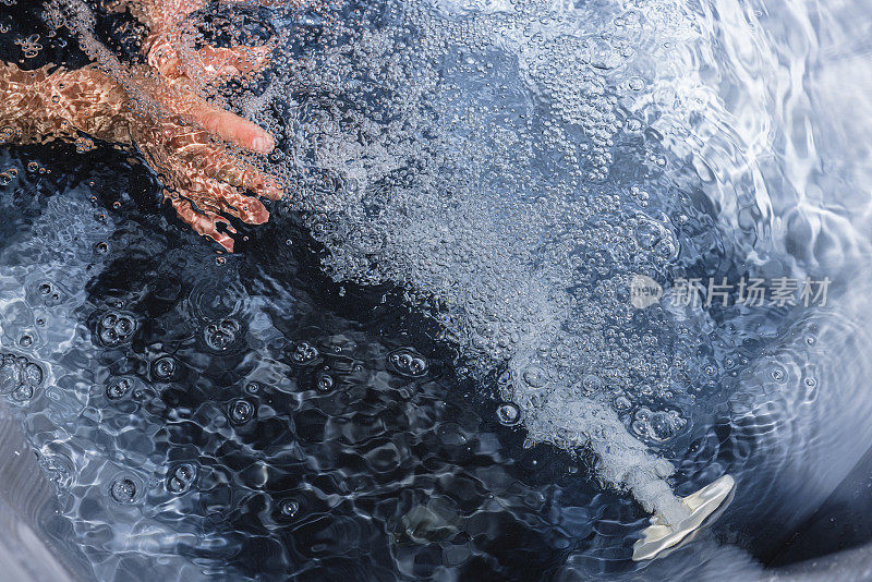 一名男子把手放在热水浴缸上，面对着从水疗中心喷水口流出的气泡流。