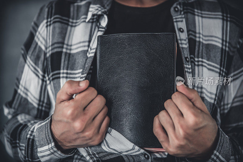 年轻人把圣经藏在衬衫里。基督教的概念。