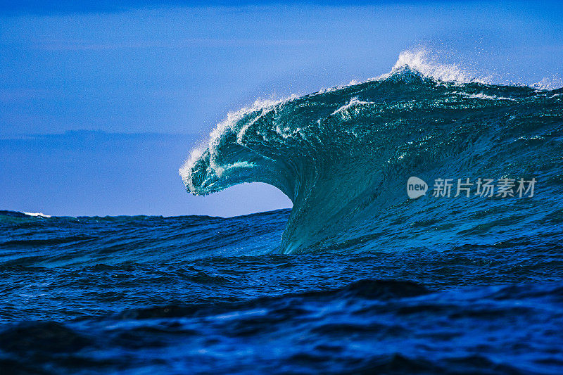 巨大的蓝色弯曲波浪在开阔的海洋上冲破一个浅海礁