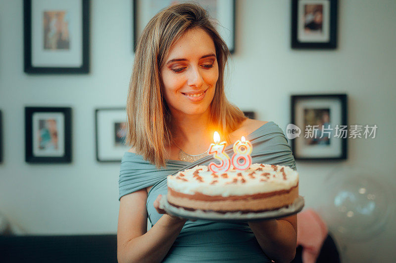 快乐的女人拿着她的生日蛋糕在家里庆祝