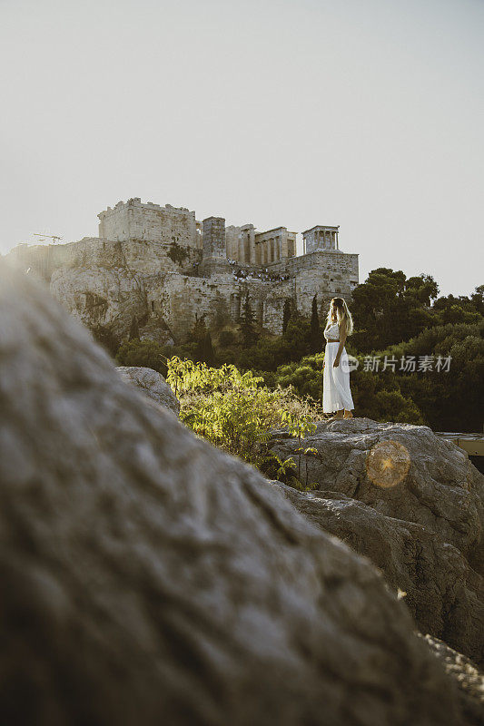 希腊雅典，日落时分，一名年轻女子在阿略帕古斯山上欣赏雅典卫城遗址的景色