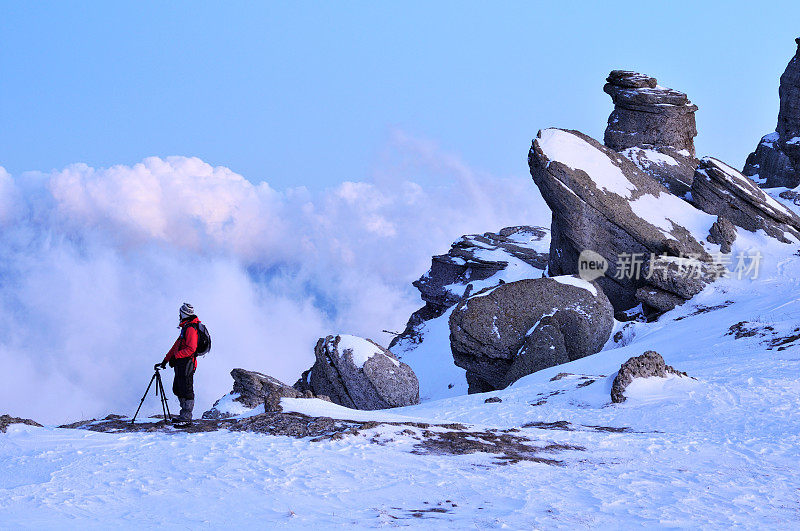 一个背包客站在冬天山上的一块岩石上