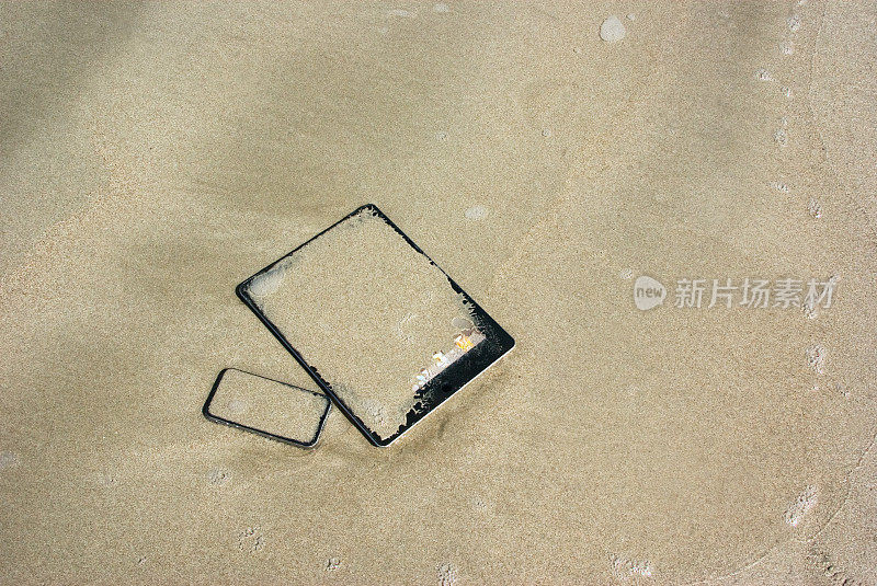 哦;数字平板电脑和智能手机淹没在潮湿的沙子里