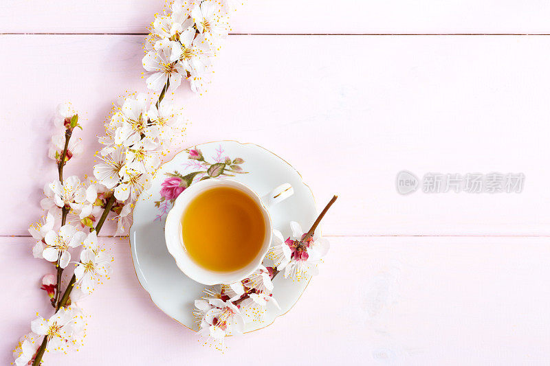 淡粉色的木桌上放着一杯茶和春花。