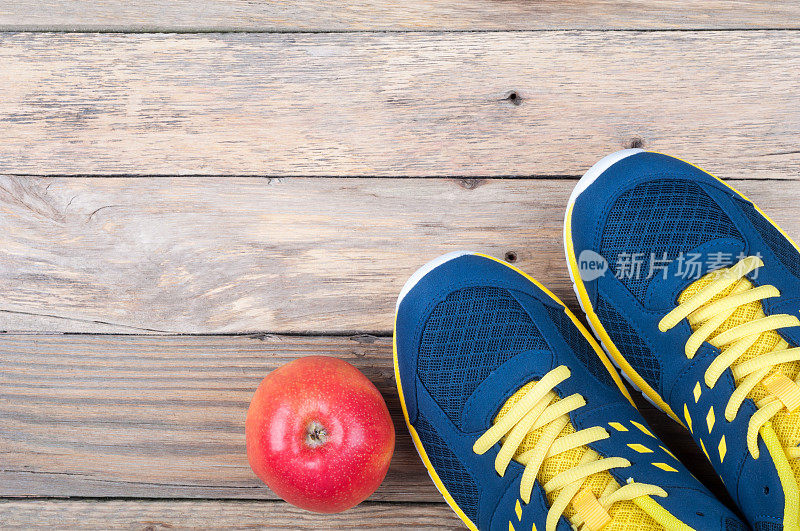 木制背景上的运动鞋和苹果。运动器材俯视图。健康的生活方式的概念