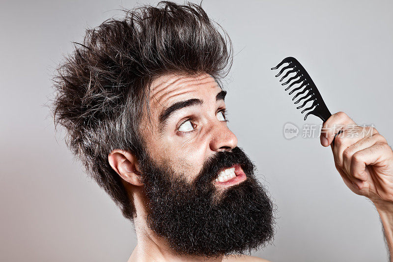头发凌乱的大胡子男人盯着一把破烂的梳子