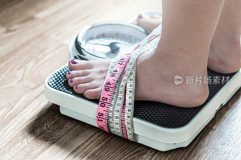 双脚用卷尺绑在秤上。对减肥上瘾和痴迷。厌食症和饮食失调的概念。
