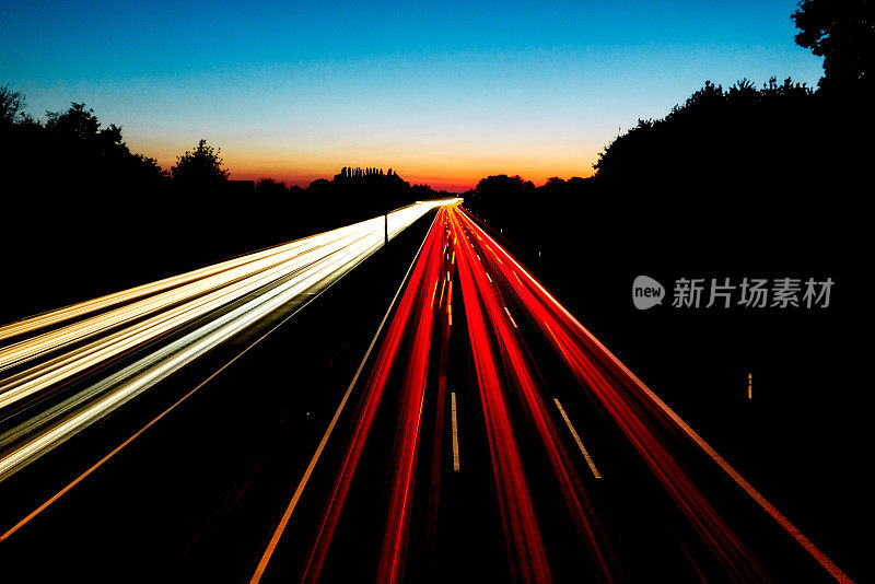 德国盖尔森基兴A2高速公路的长曝光图像，背景是红色和白色的光迹和彩色的日落