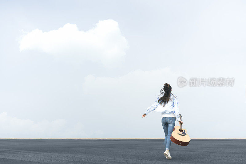 年轻风格的女人拿着吉他在天空中行走