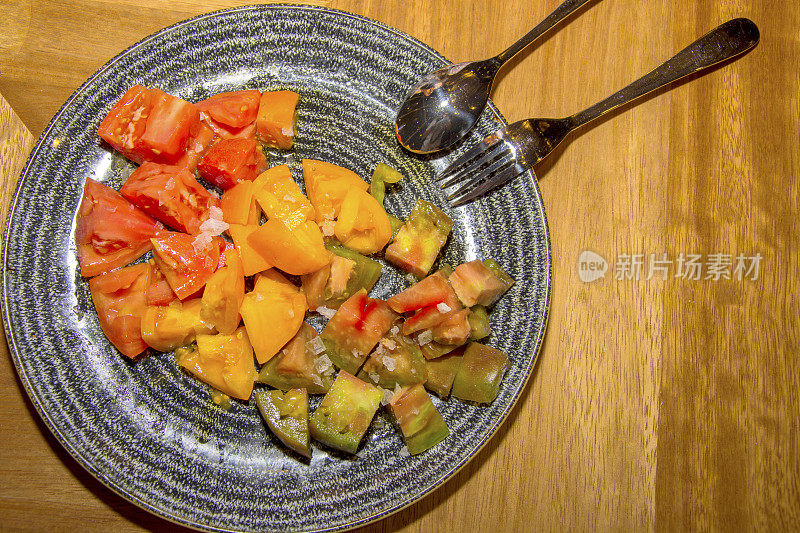 一盘用绿、黄、红三种颜色调味的西红柿做成的沙拉。用钢勺和钢叉来上菜。水平