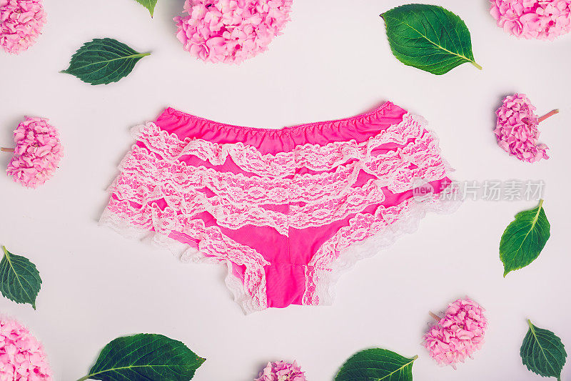 俯视图女性性感蕾丝内裤和粉红色紫藤花和绿色的叶子在白色的背景。内衣，漂亮的内衣衣服。时尚的概念。