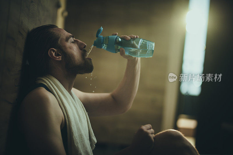 精疲力竭的男运动员在训练后在更衣室饮水。