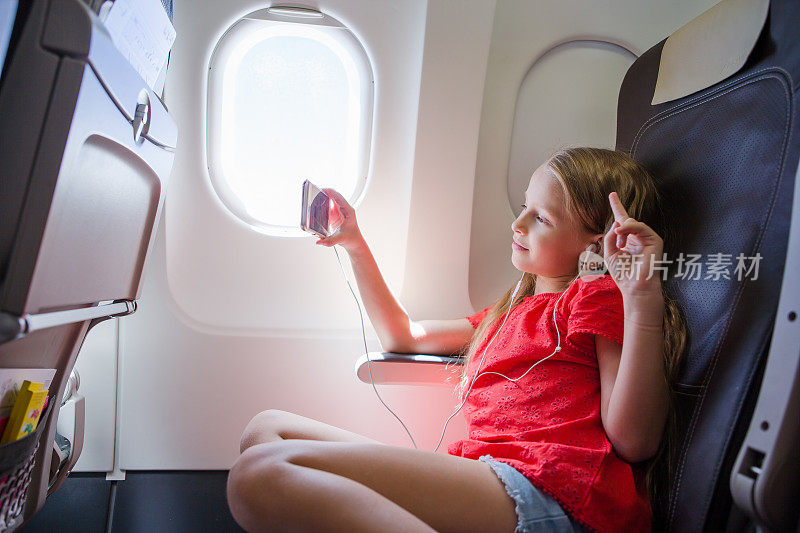 可爱的小女孩乘飞机旅行。坐在飞机窗口附近的小孩