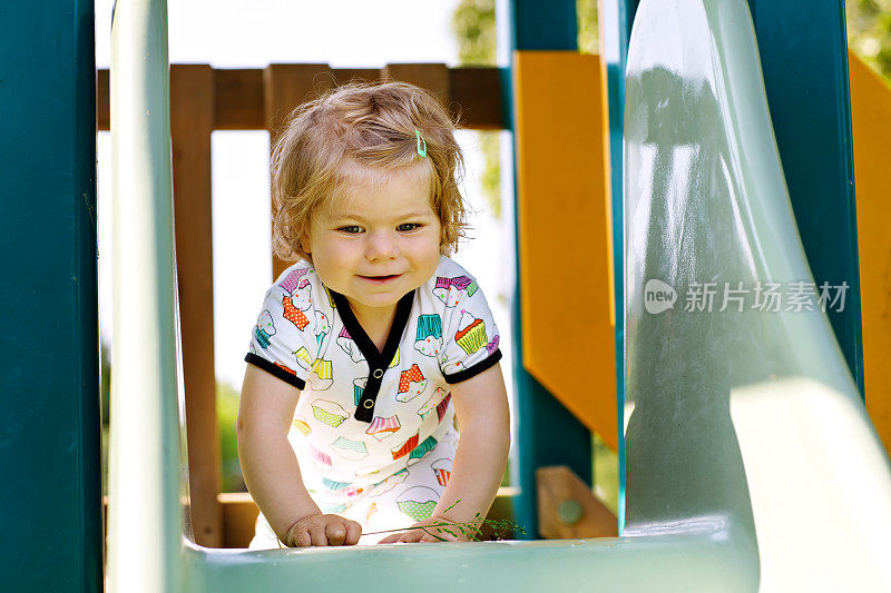 快乐的金发小女孩有乐趣和滑在户外操场上。积极有趣的宝宝宝宝微笑。