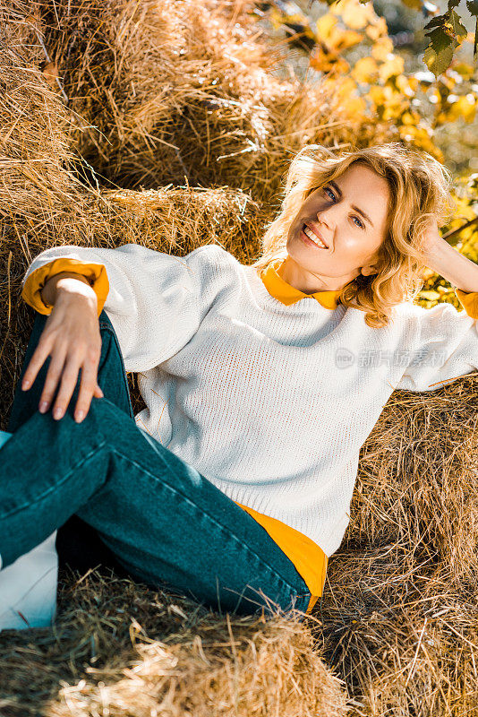 微笑的女人看着相机，躺在牧场的干草堆上