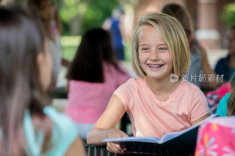 可爱的白人小女孩戴着牙套在学校和不同的朋友群学习