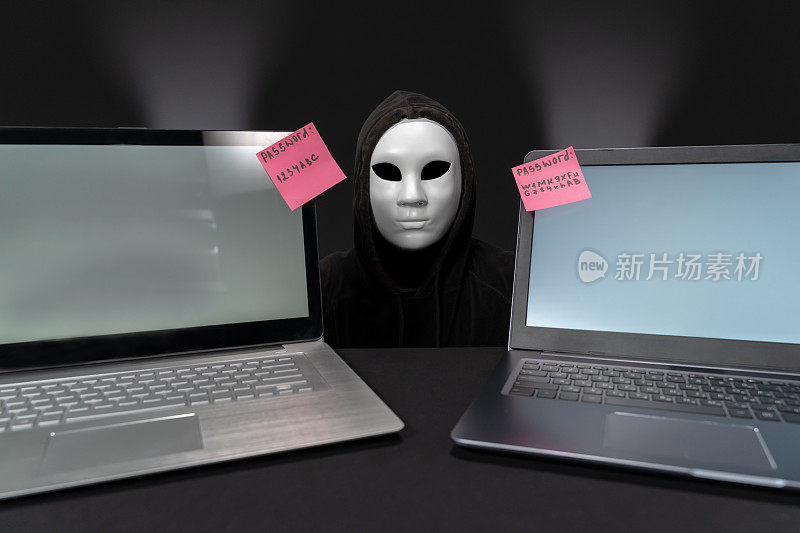蒙面黑客在两台笔记本电脑之间，屏幕上有密码