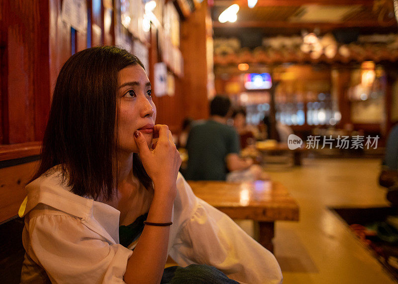 在日本传统的居酒屋餐厅，一名年轻女子正在看墙上的菜单