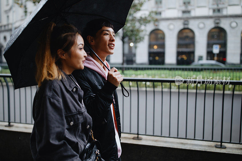 近距离拍摄一对年轻夫妇撑着伞，走在下雨的街道上
